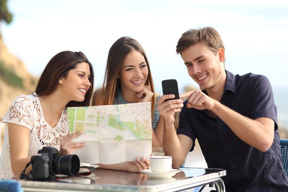 Three friends staring at a map and reviewing on their mobile phone.