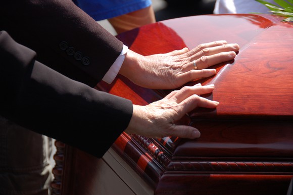 two hands touching casket, presumably at funeral