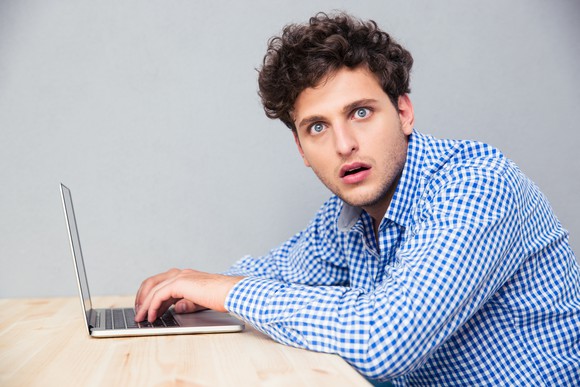 A surprised man sitting at a laptop.