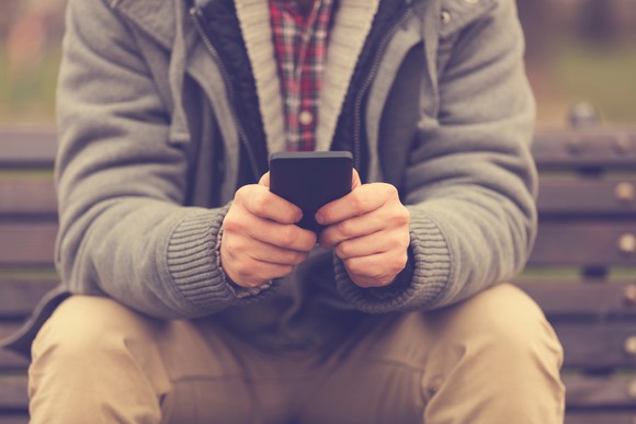 A person sitting uses his smart phone to text someone.