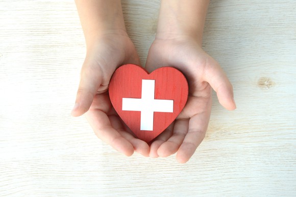 A person holding a red plastic heart with a white cross painted on it.