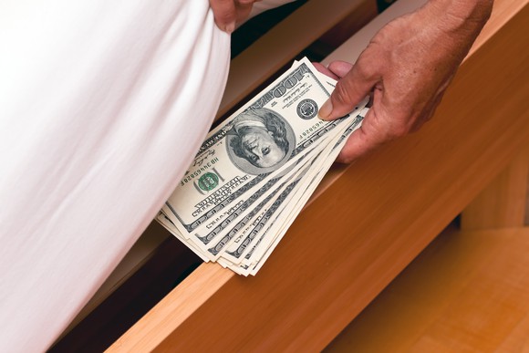 A person putting cash under their mattress.
