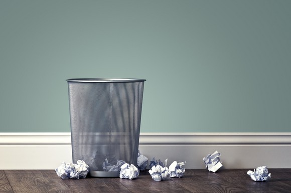 A photo of a trash can with crumbled up paper lying nearby.