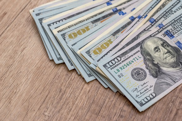 A pile of dollar bills fanned out on top of a wooden desk