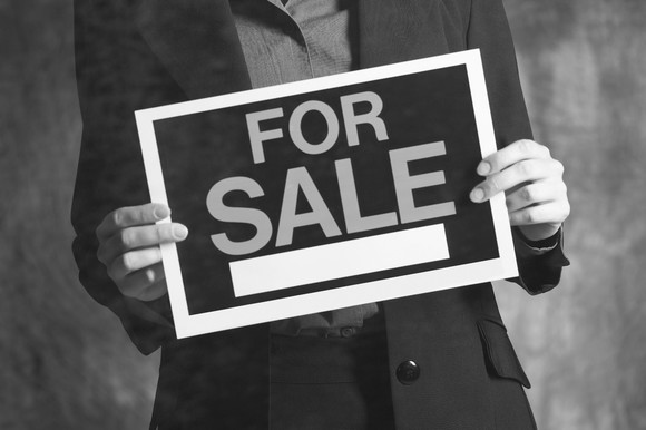 A businessman holding a for sale sign. 