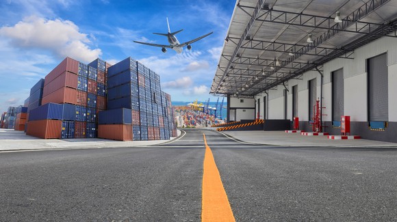 Cargo plane taking off from airport above a warehouse and stacked shipping containers.