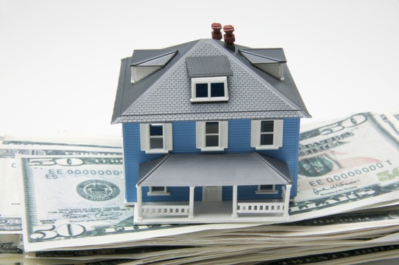 A toy house sits atop a pile of money.