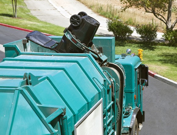 Robotic arm trash truck dumps a large black can.