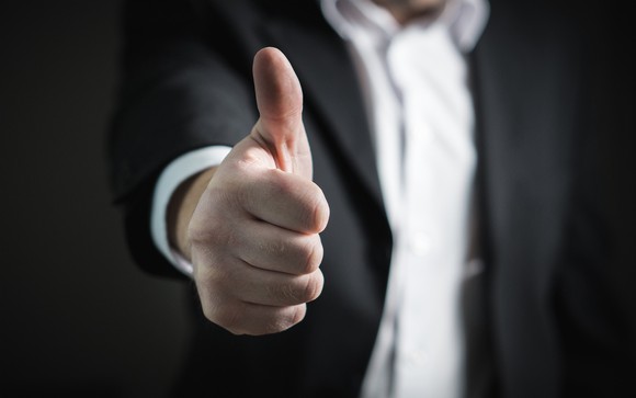 Torso of man in suit, with hand outstretched, giving thumbs up