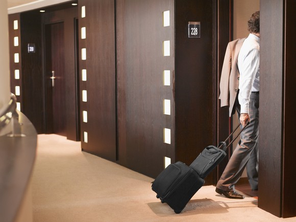 A man entering a hotel room pulling his luggage behind him.
