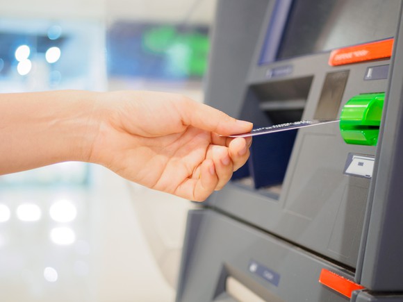 Colorful close-up of hand feeding card into ATM machine.