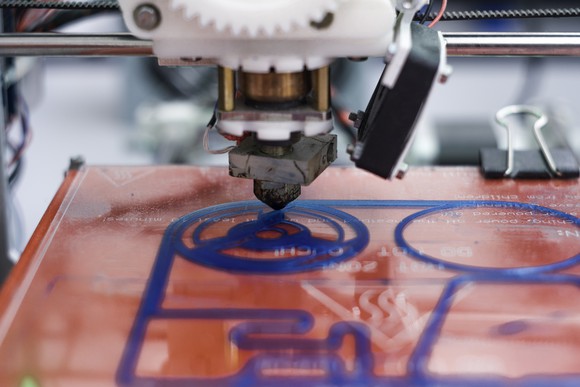 A close-up of a 3D printer just beginning to print a yet unrecognizable object.