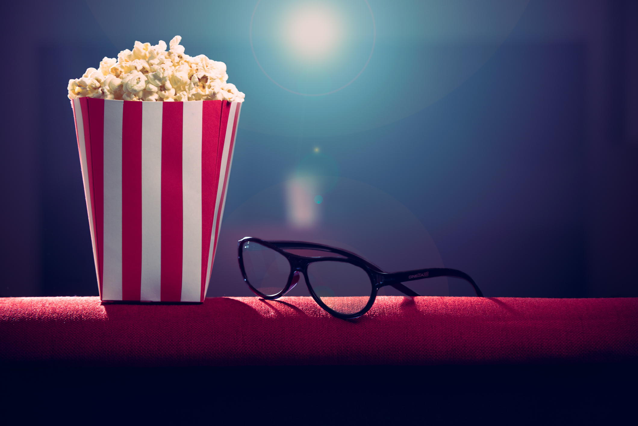 Popcorn and glasses with a movie projector in the background.