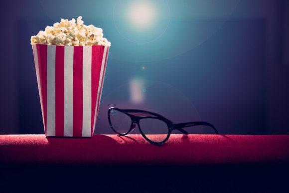 Popcorn and glasses with a movie projector in the background.