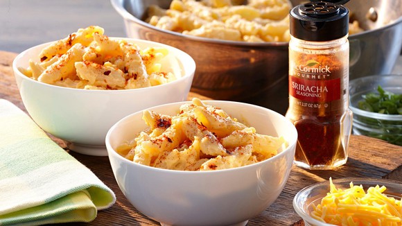 A jar of McCormick sriracha spice on a table surrounded by bowls of food.