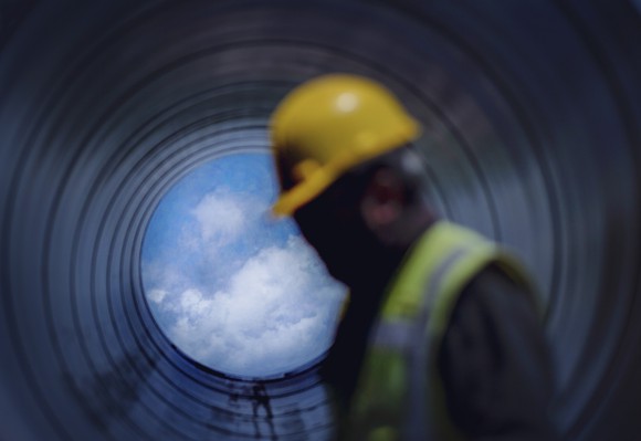 A working walking past a pipeline open to the blue sky.