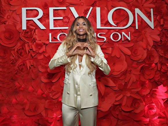 The singer Ciara standing in front of a heart made of flowers and a Revlon sign