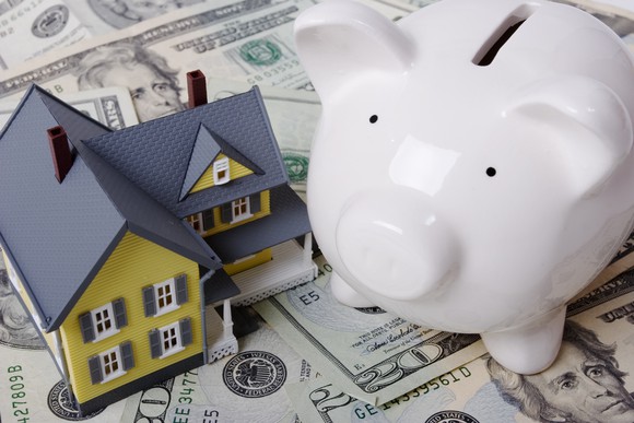 A house flanked by a piggy bank and a pile of cash, representing the estate tax.