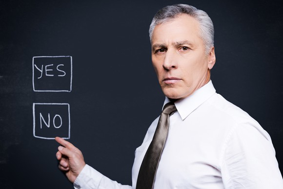 A pre-retiree pointing to a "No" answer key on a chalkboard.