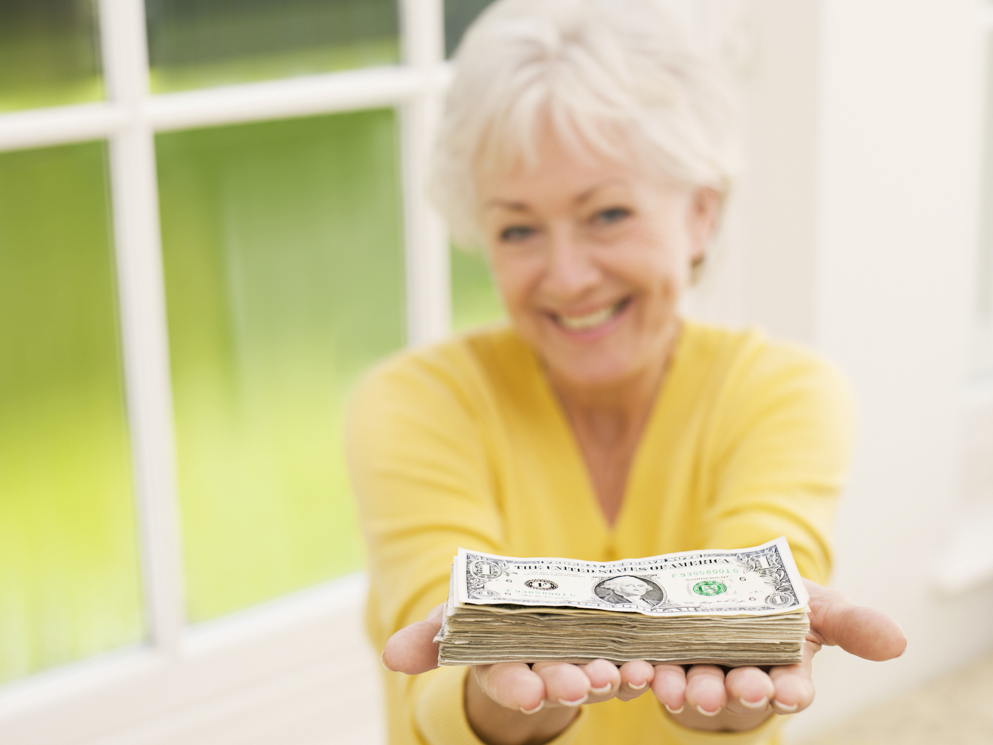 A senior woman holding out a stack of cash in her hands. 