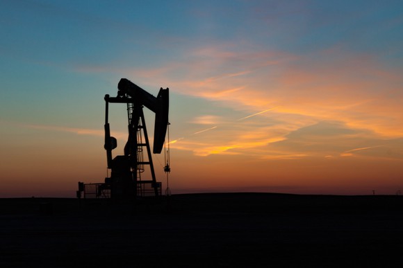 A single oil well pumpjack silhouetted against a prairie sunset.