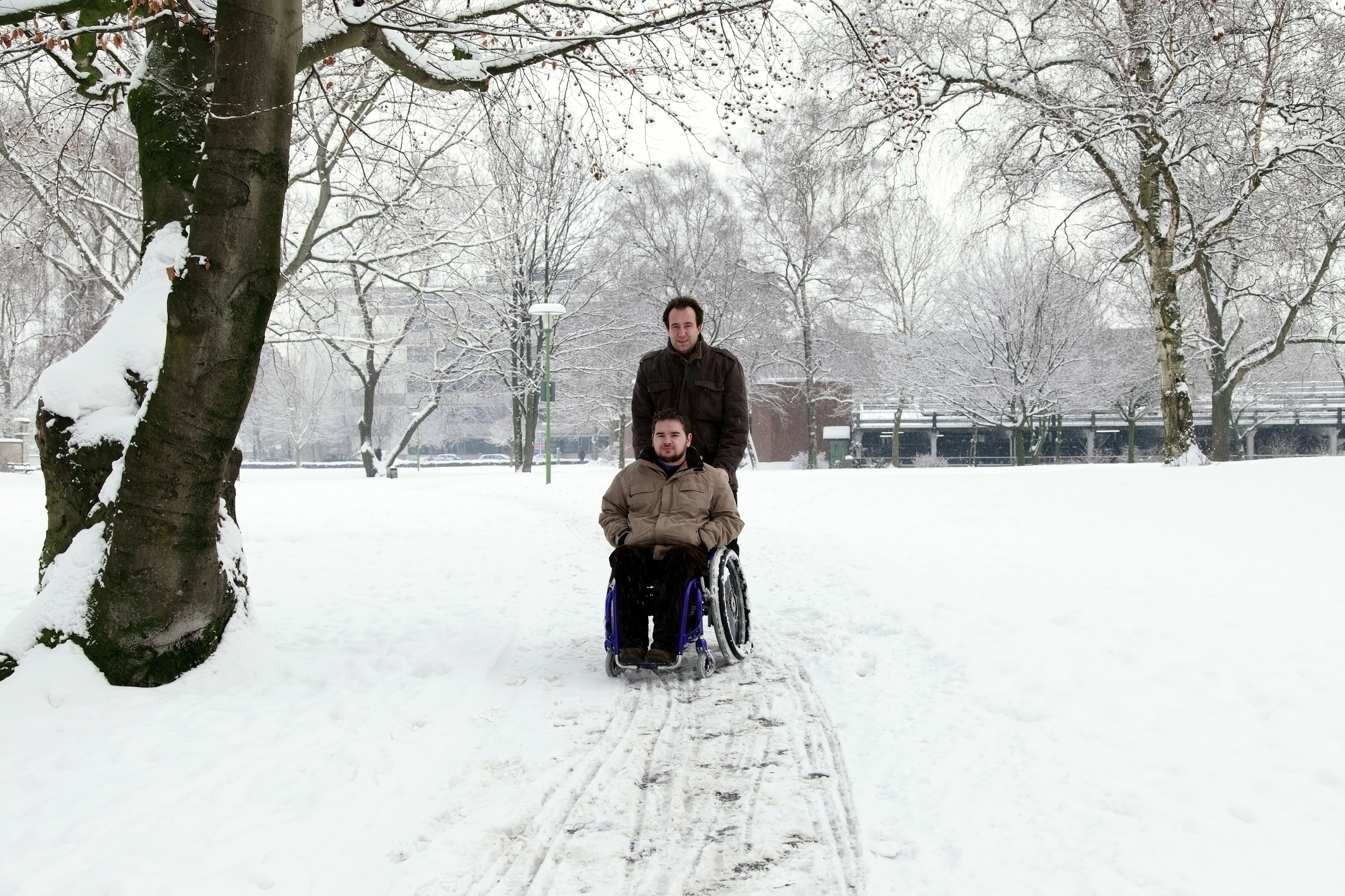 A man pushes a boy in a wheelchair through the snow.
