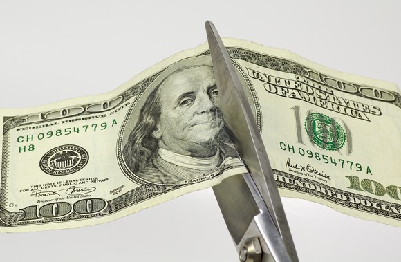 Scissors cutting through a hundred dollar bill, representing cost-cutting.