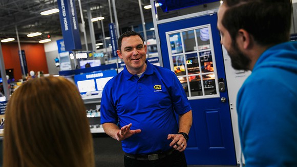 A Best Buy customer service person assisting two customers.