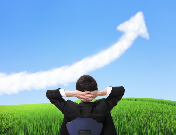 A person in a business suit looks at a cloud shaped like an upward-sloping arrow.