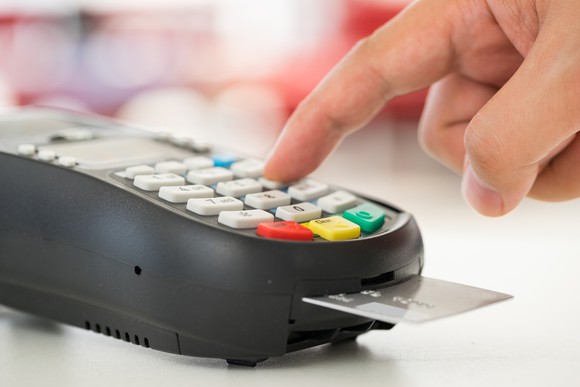 A hand hovers over a credit card machine, with a card inserted into the chip reader.