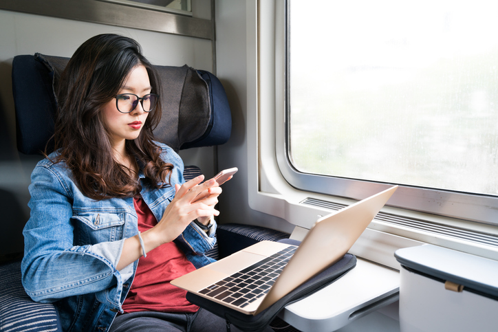 A woman working on a computer and smartphone while riding a train