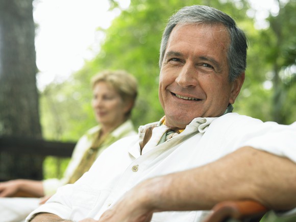 An older couple, smiling and sitting outdoors.
