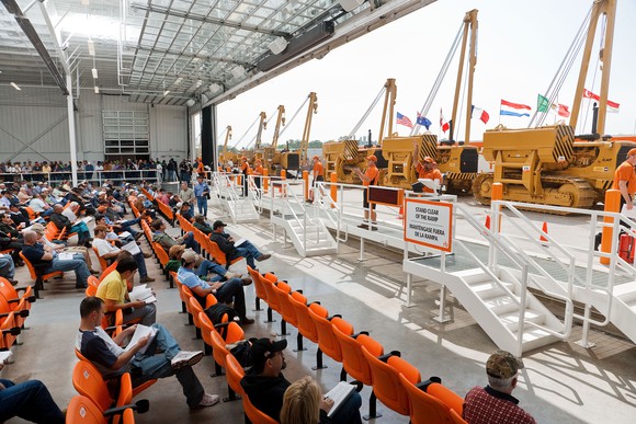 Auction site with a collection of heavy equipment on display and rows of bidders sitting in the audience.