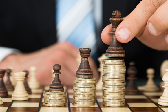 A man in a suit placing chess pieces on top of stacks of coins of varying heights arranged in accordance with their value.