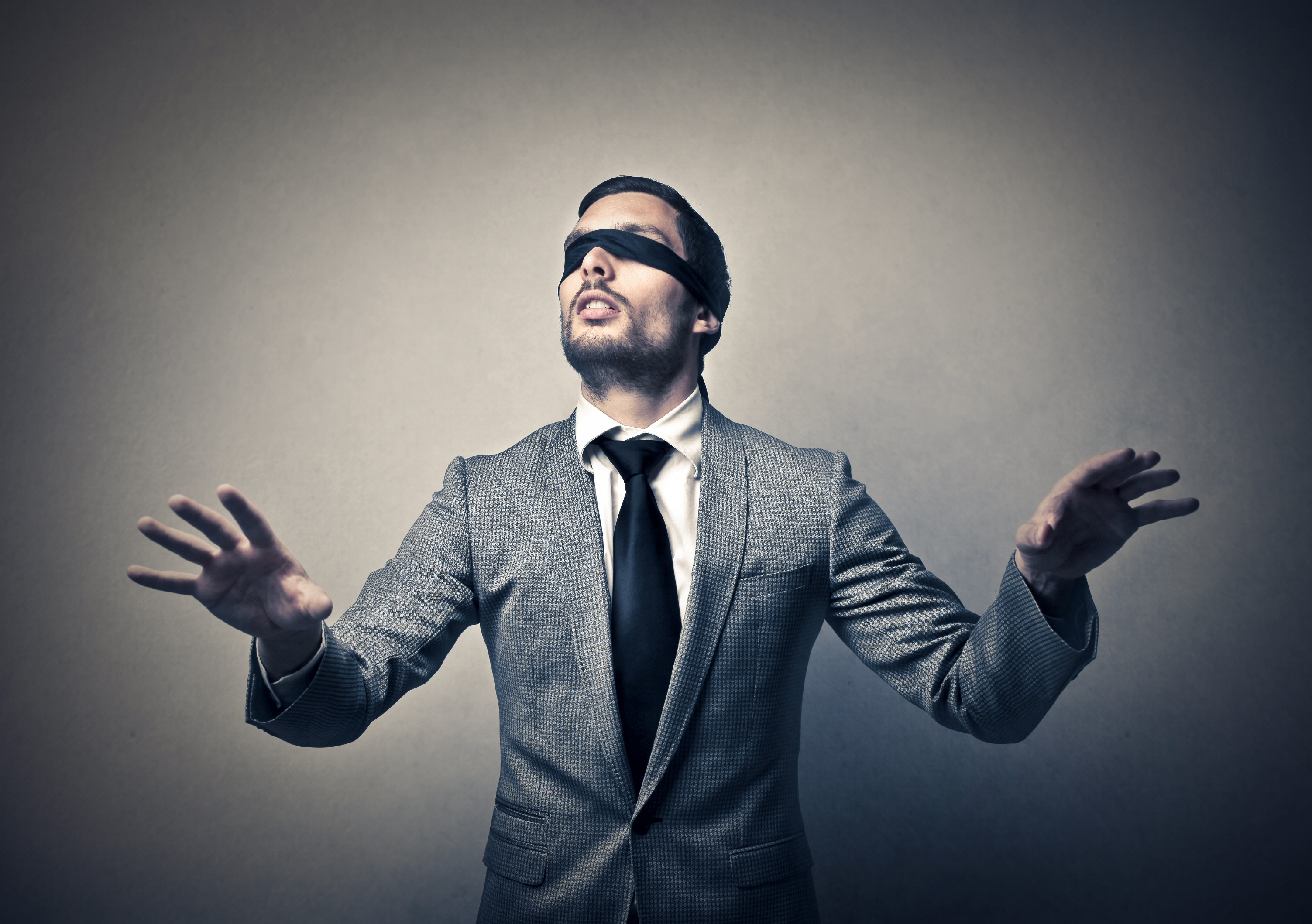 Blindfolded man in a suit feeling way around a room.