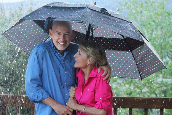 A senior couple smiling under an umbrella in the rain.