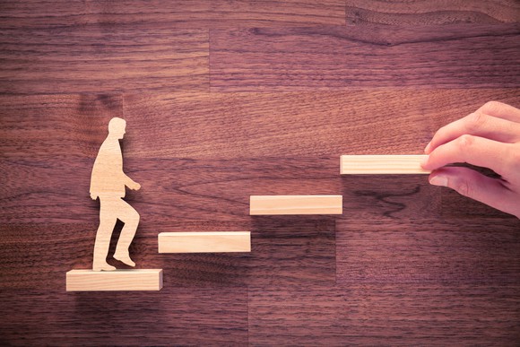 A wooden figure climbs wooden steps.