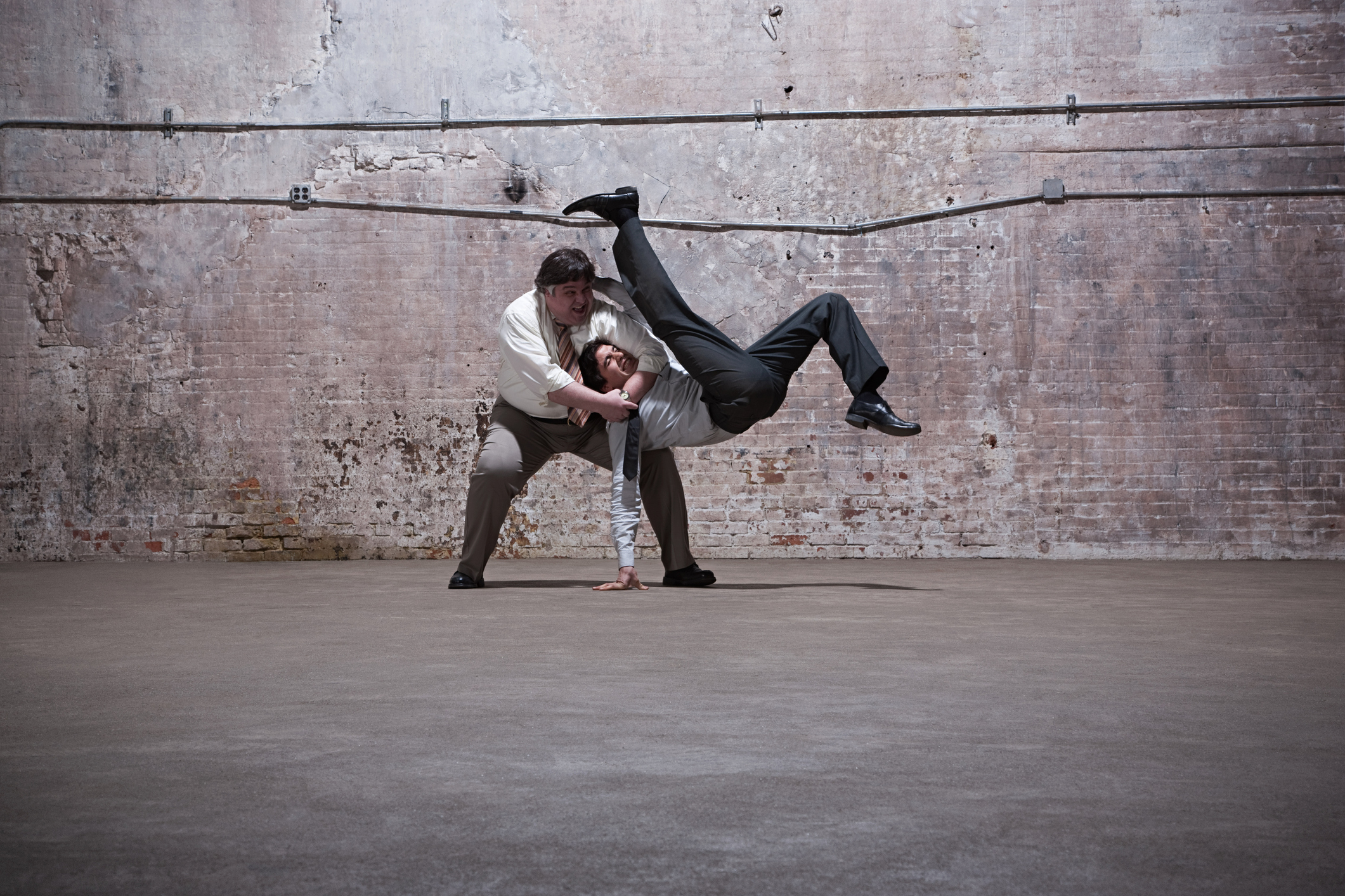 Two middle-aged men in business attire fighting in warehouse.