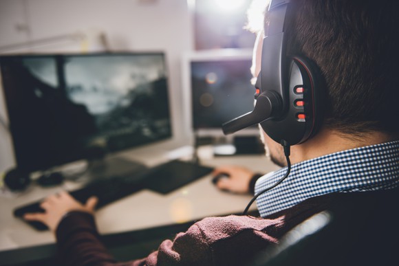 Man wearing headphones and playing a video game on a desktop computer.