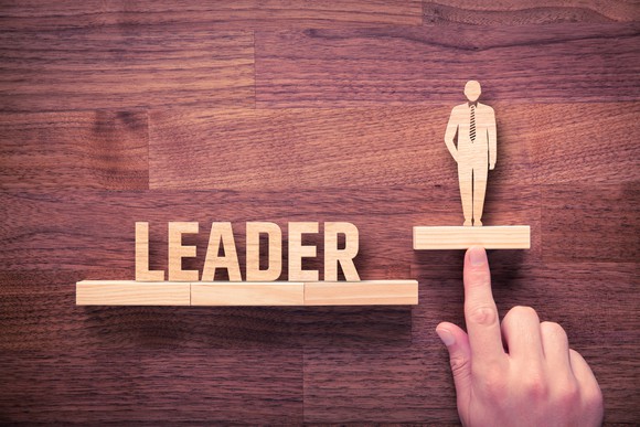 Wood carvings of the word "leader" and a man, with a finger pointing to the man.
