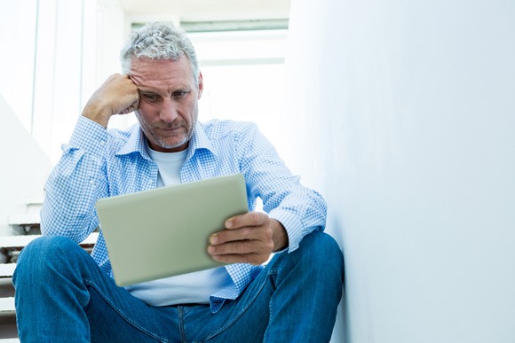 An older man with a worried expression looks at a tablet.