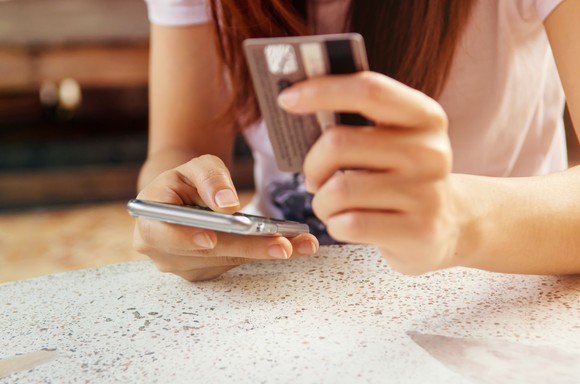 Person holding credit card in one hand, smartphone in the other.