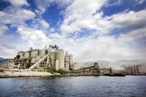 Cement plant at shoreline with blue sky and clouds.
