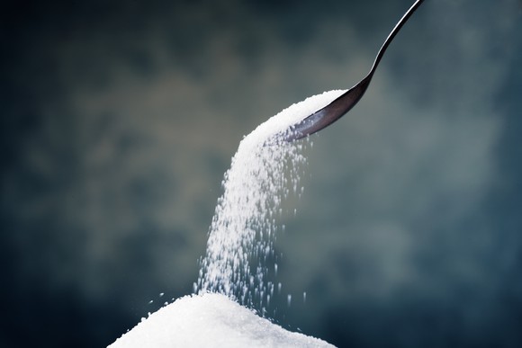 A spoon dumping sweetener onto a pile.