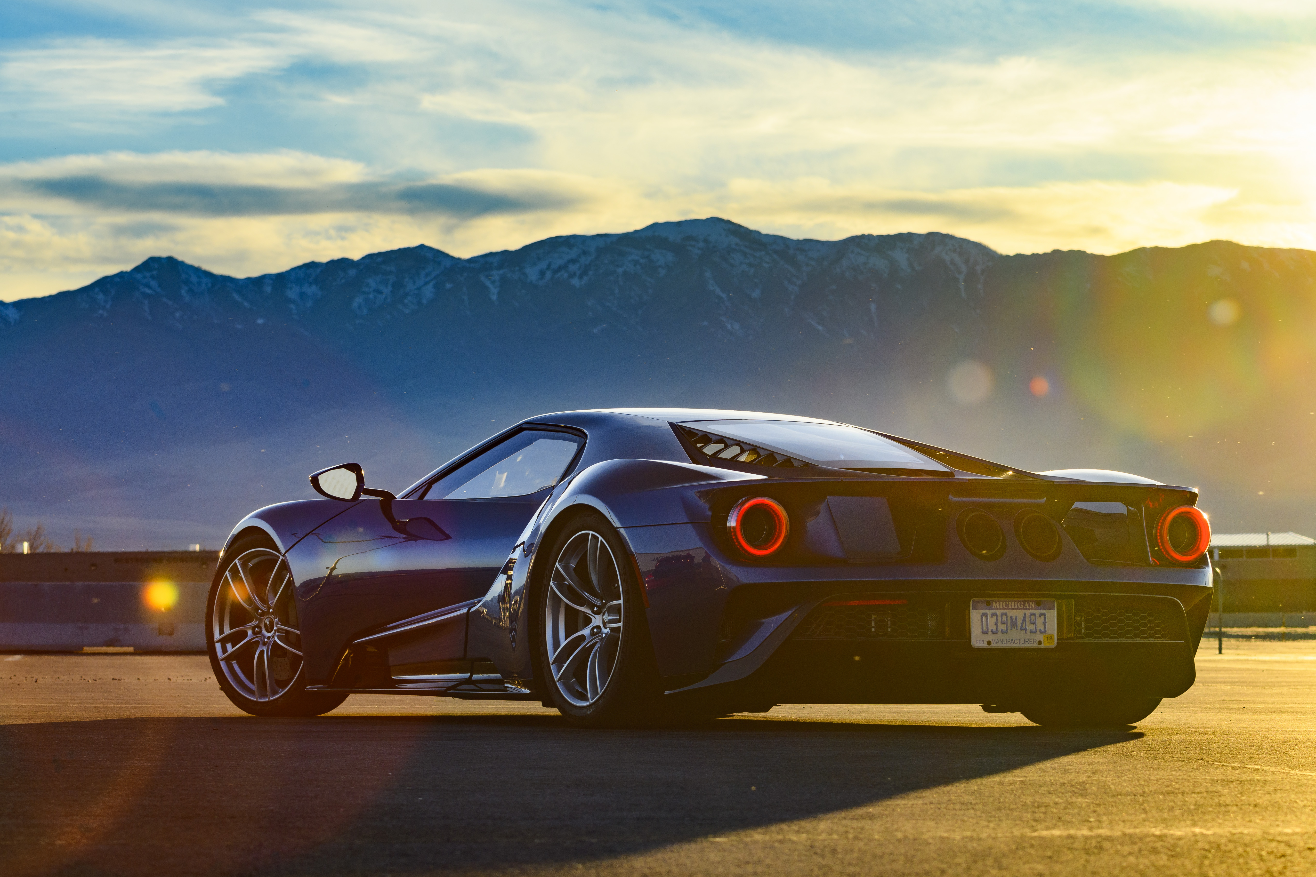 The rear view of a Ford GT, with mountains and the sun in the background.