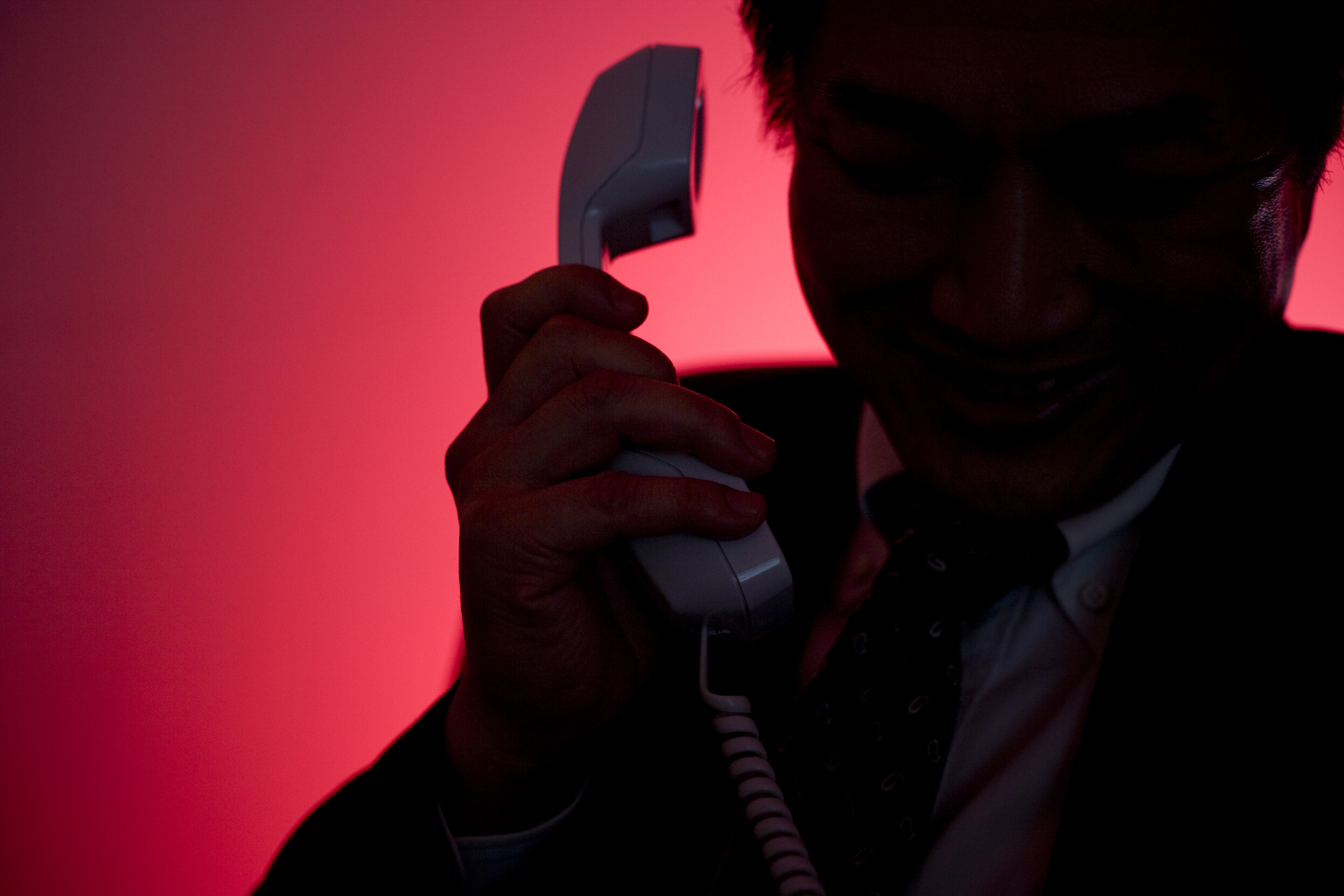 A man silhouetted against a red background raises a phone to his ear.