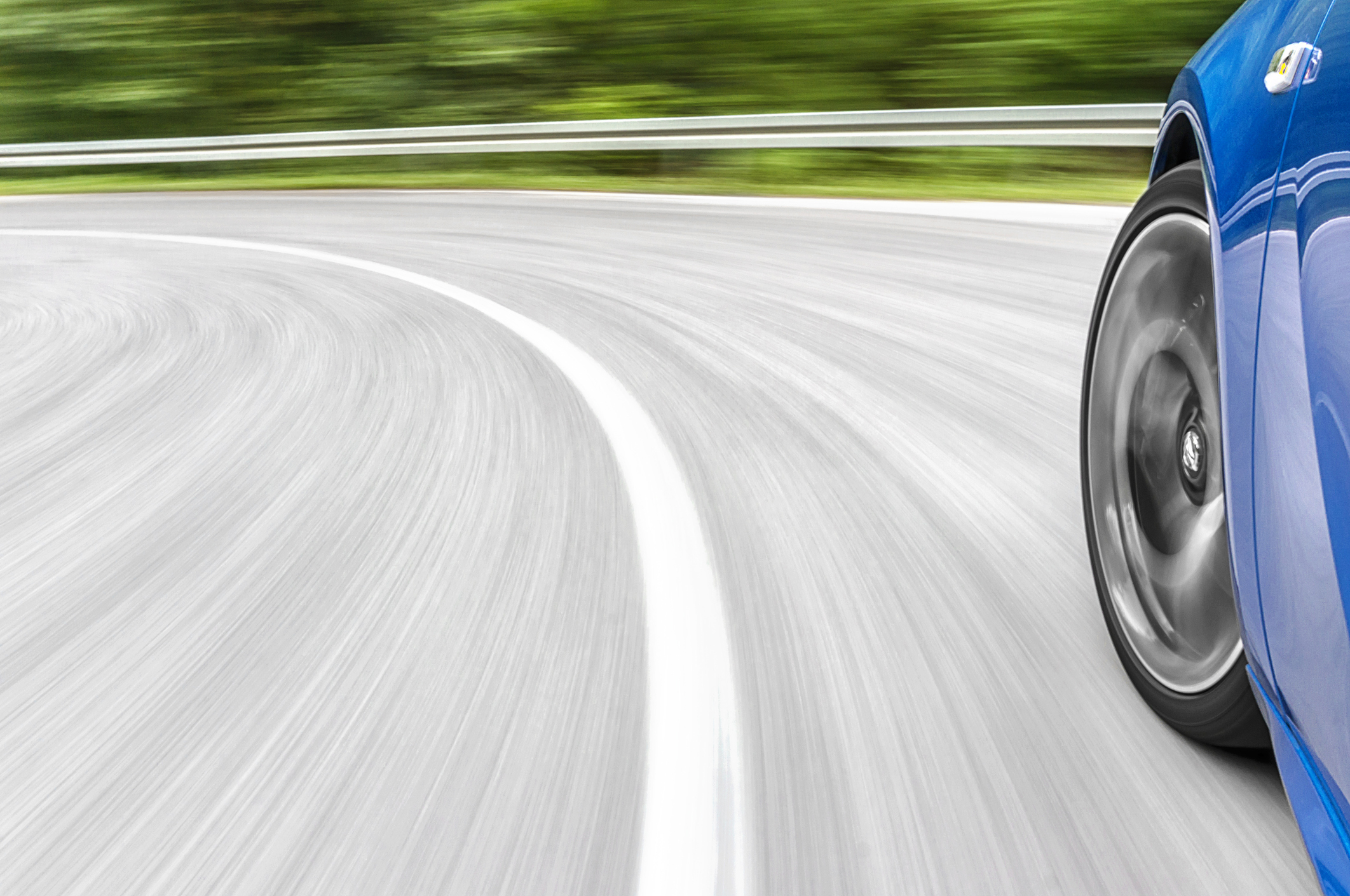 Motion blur shot of  a car driving fast on the road, showing the front corner of the car from a side view.