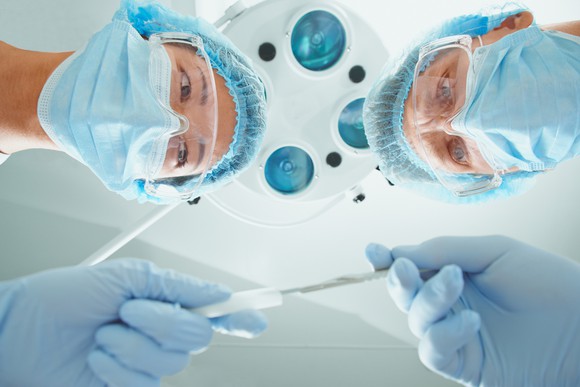 A nurse passes a scalpel to a surgeon, from the perspective of someone lying on an operating table.