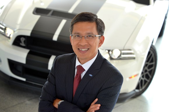Thai-Tang is shown standing before a white Ford Mustang.