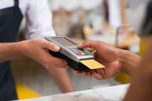 A merchant holds a credit card machine for a customer, who presses a key with his card inserted.